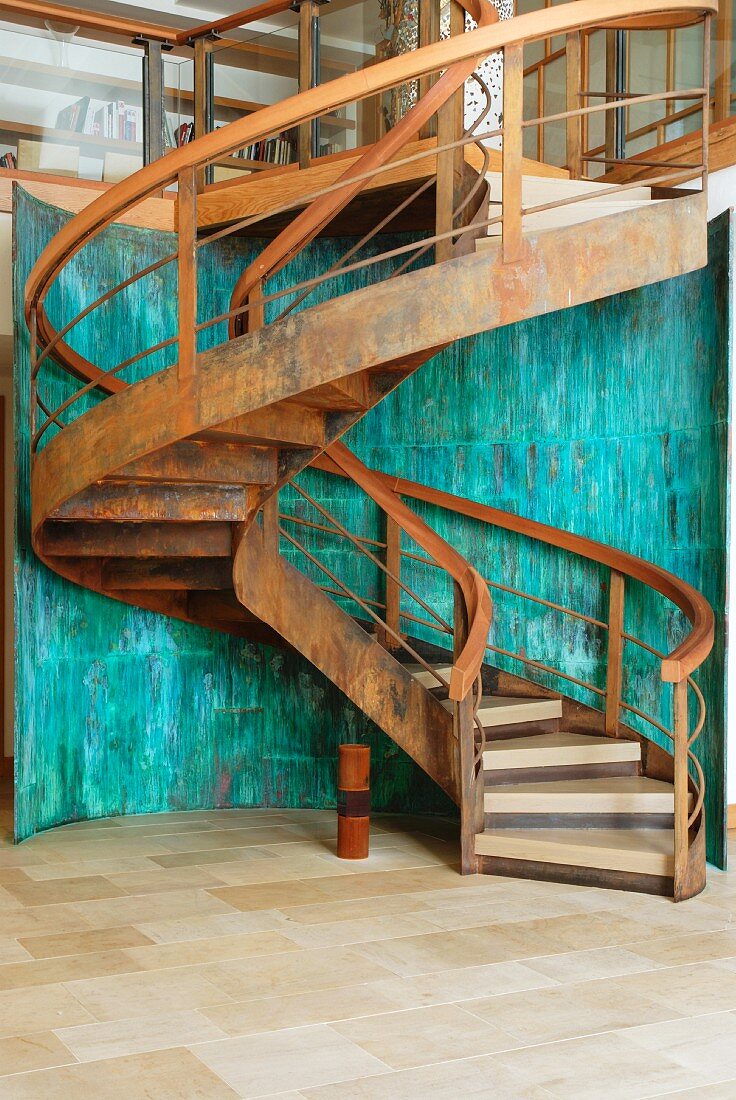 Curved staircase in corten steel with wooden treads in front of curved wall of verdigris copper panels