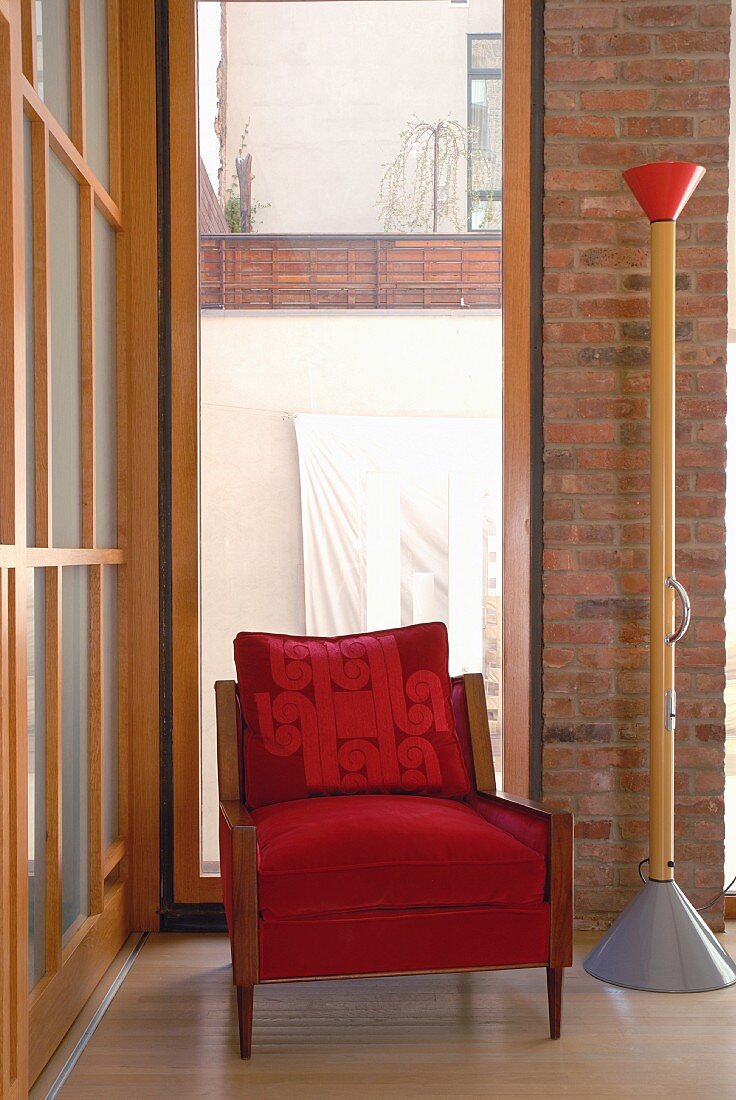 Roter Sessel mit Holzgestell neben postmoderner Stehlampe in Zimmerecke vor raumhohem Fenster