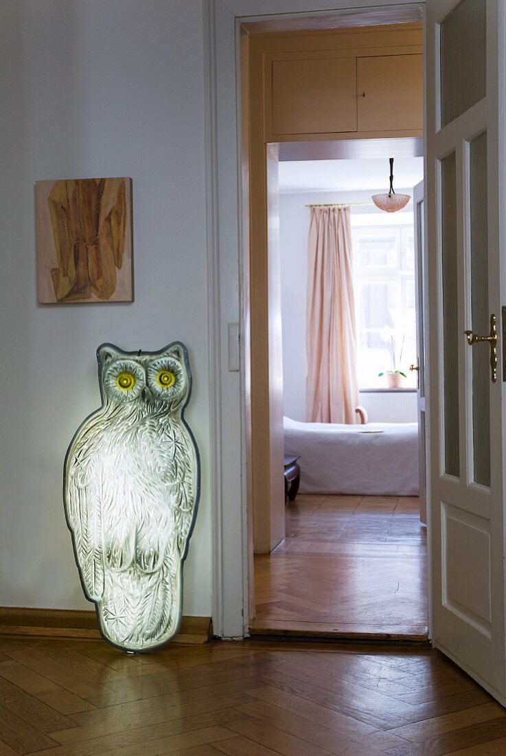 Eulenfigur aus Metall an Wand lehnend neben offener Tür und Blick ins Schlafzimmer