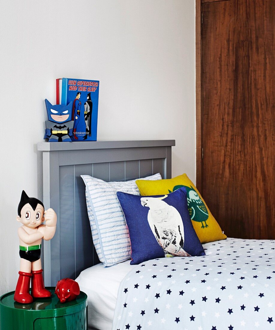 Action figure on side table next to single bed with wooden headboard painted grey in teenager's bedroom