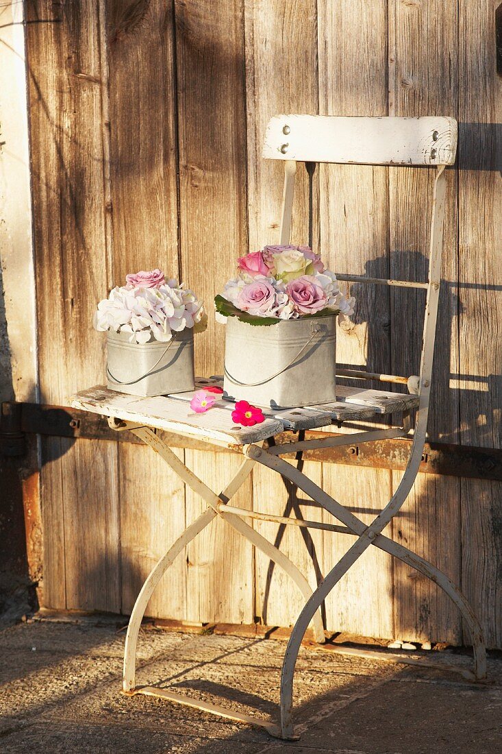 Festive flower arrangements in small zinc buckets on weathered, vintage garden chair against wooden wall