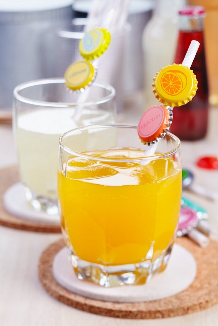 Orangen- und Zitronensaftgläser mit Trinkhalmen, verziert mit Kronkorken und dem entsprechendem Fruchtmotiv