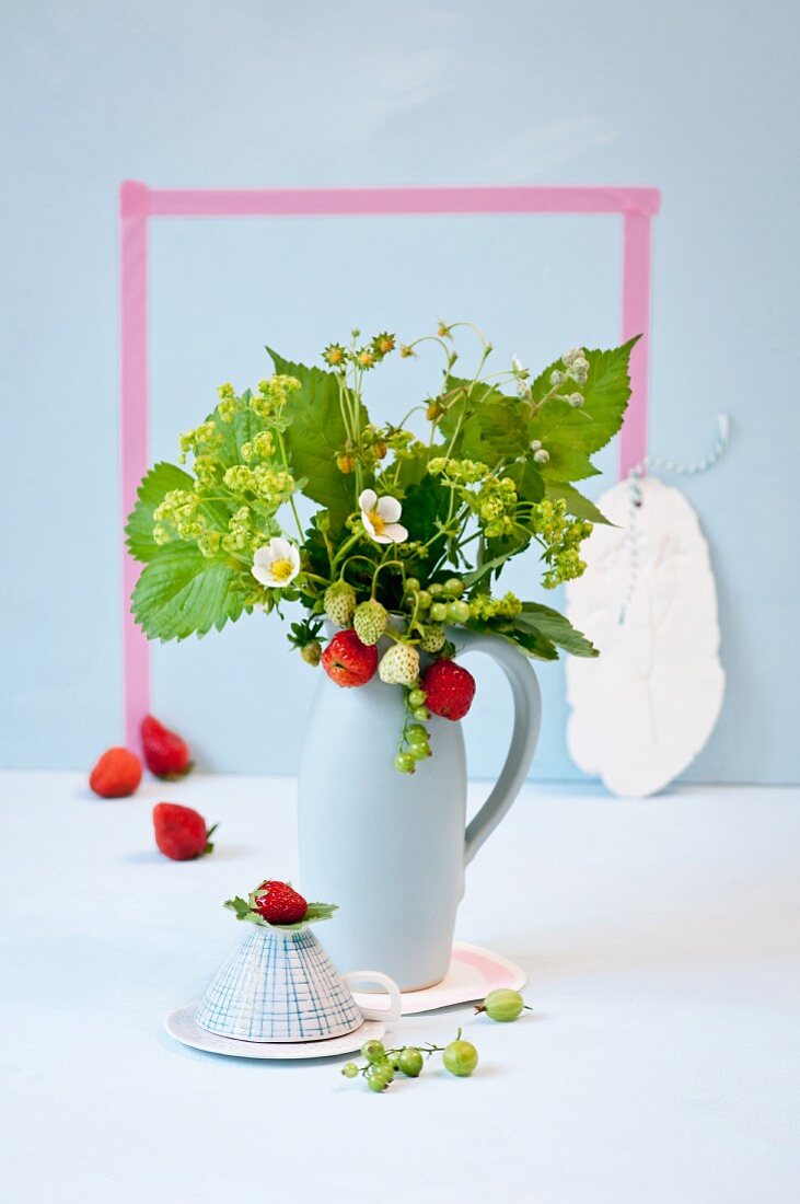 Hellblauer Krug mit frischen Erdbeeren, Erdbeerblüten und Frauenmantel