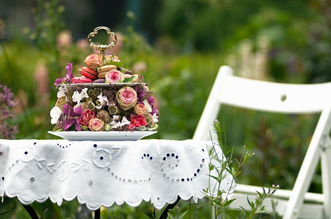 Romantic cake stand decorated with roses and other flowers on white broderie anglaise table cloth in summery garden