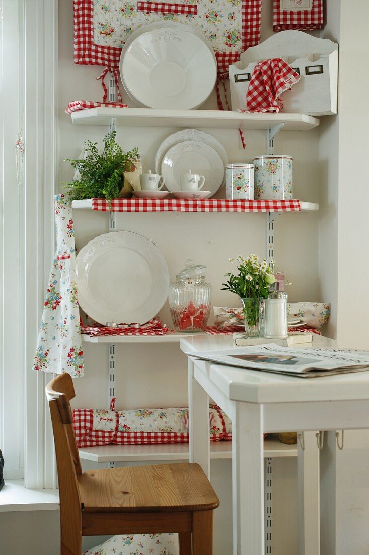 Sales room with white, country-style china displayed on shelves decorated with red and white gingham fabric