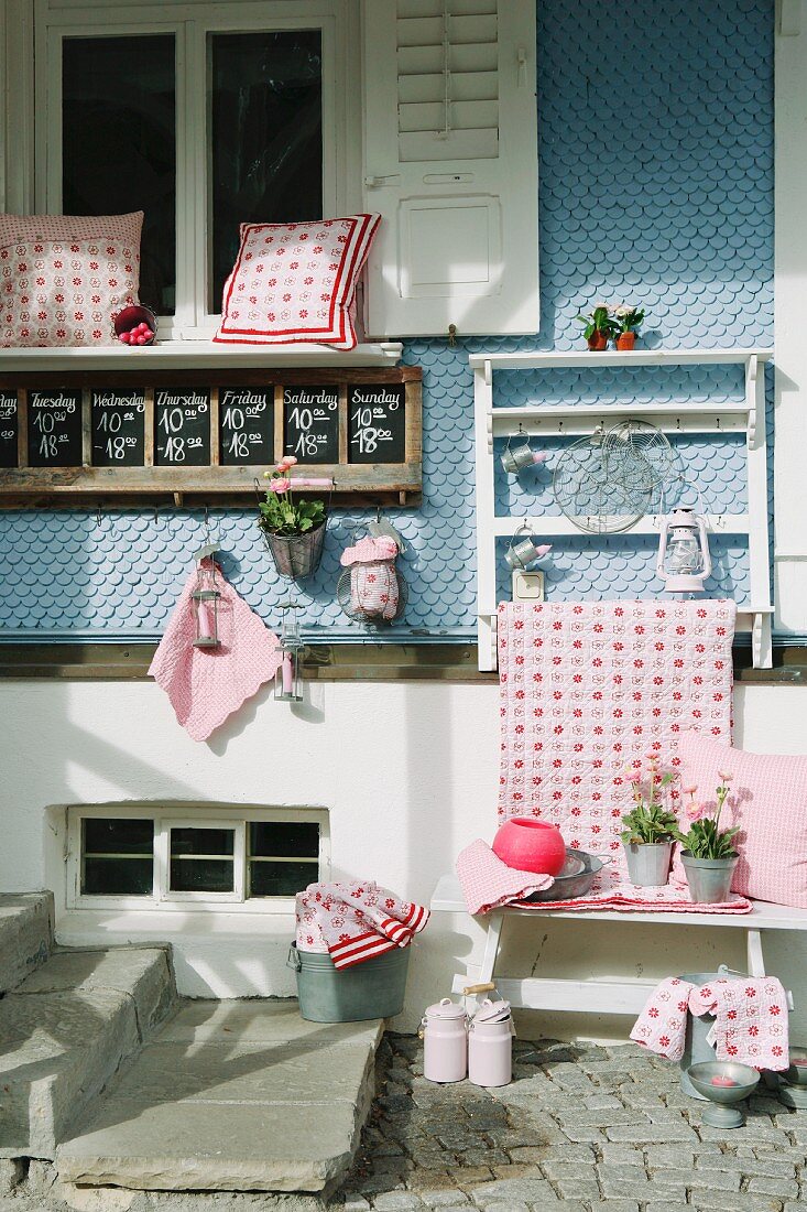 Red and white cushions and other country-style home accessories decoratively displayed for sale in front of pale blue wooden facade