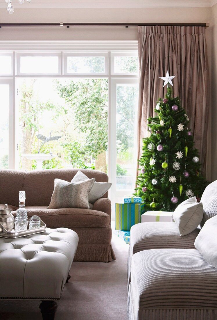 Sofa set and tray on ottoman in front of Christmas tree next to window