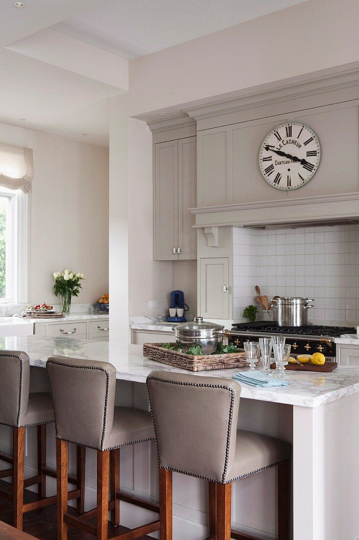 Breakfast bar and leather-covered bar stools in elegant, open-plan country-house kitchen with vintage wall clock