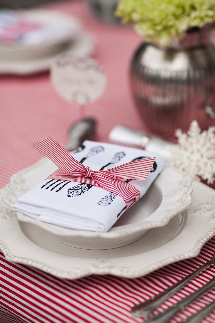 Porzellanteller mit Reliefverzierung auf rot-weiss gestreifter Tischdecke und Serviette mit Geschenkband