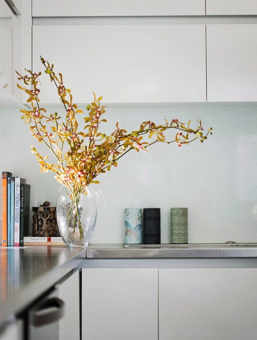Detail of fitted kitchen - glass vase of flowering branches on stainless steel worksurface, wall units and base units with white doors