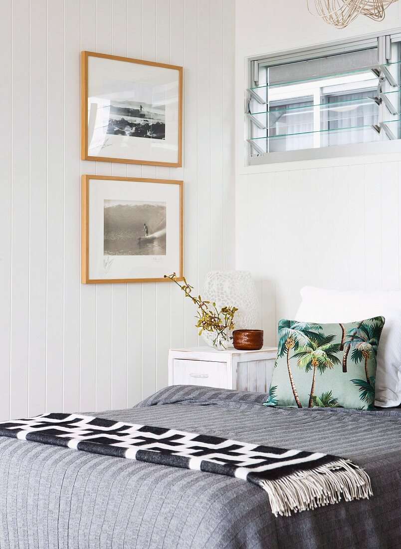 Black and white geometric blanket and grey bed linen on bed below glass louvre window in corner