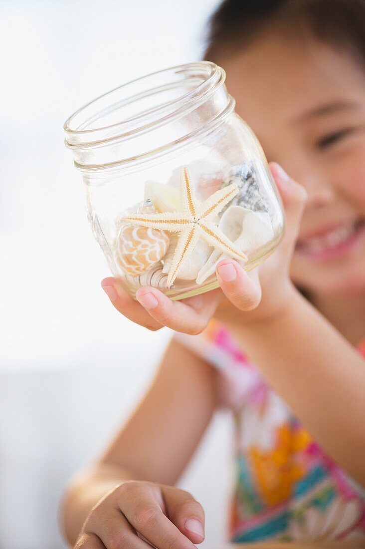 Little girl holding glass jar of starfish and seashells