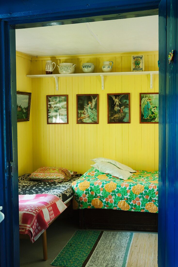 View into bedroom with twin beds, yellow-painted walls and framed religious pictures
