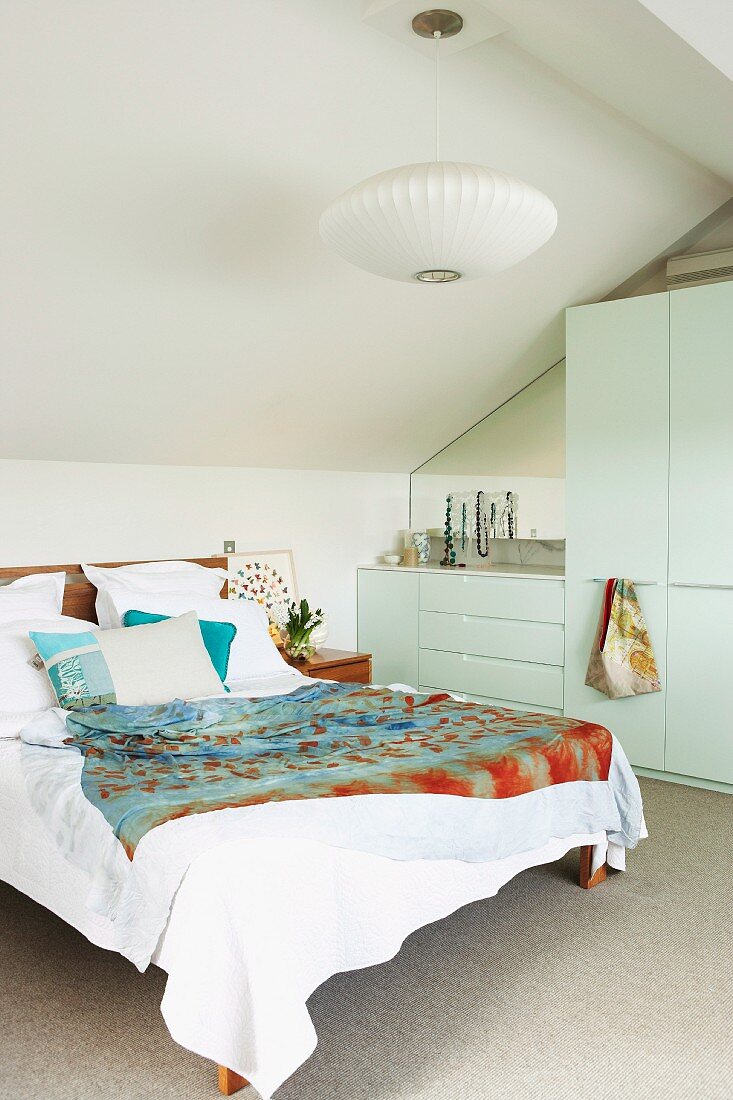 Double bed next to wardrobe in white, modern bedroom with sloping attic ceiling