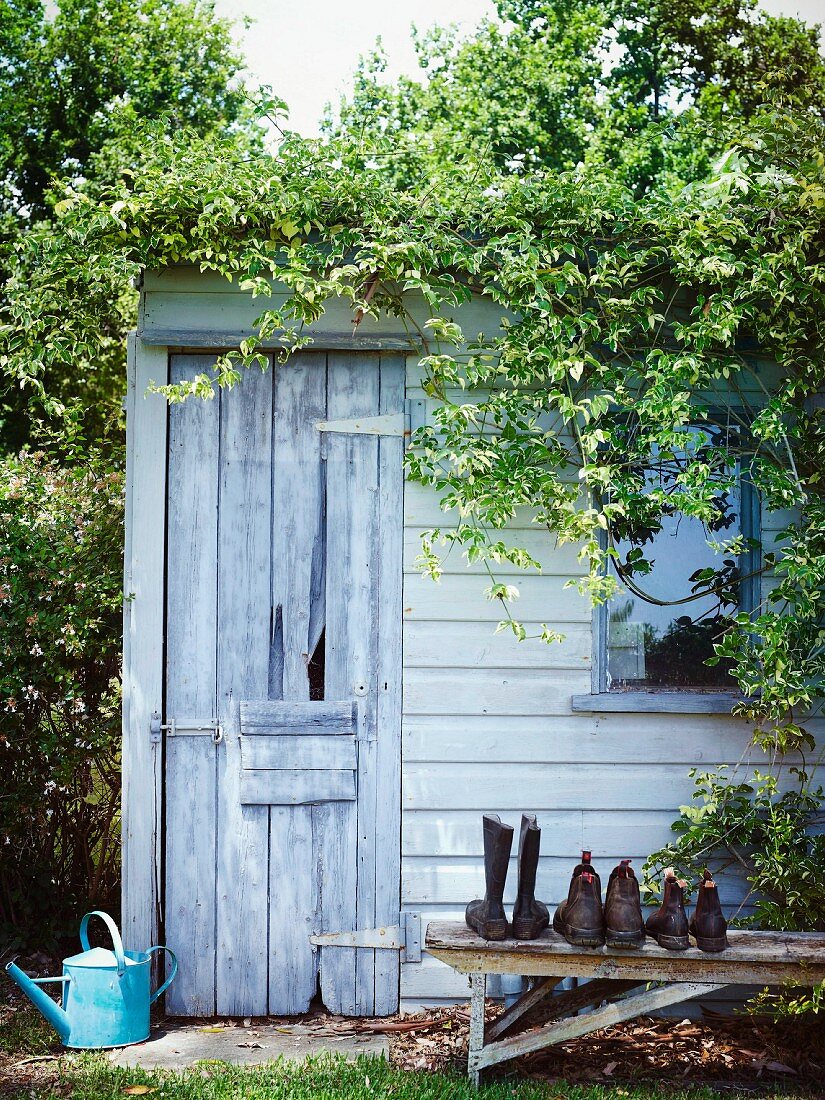 Gartenhäuschen mit rustikaler Holztür und verwitterte Holzbank mit Schuhen