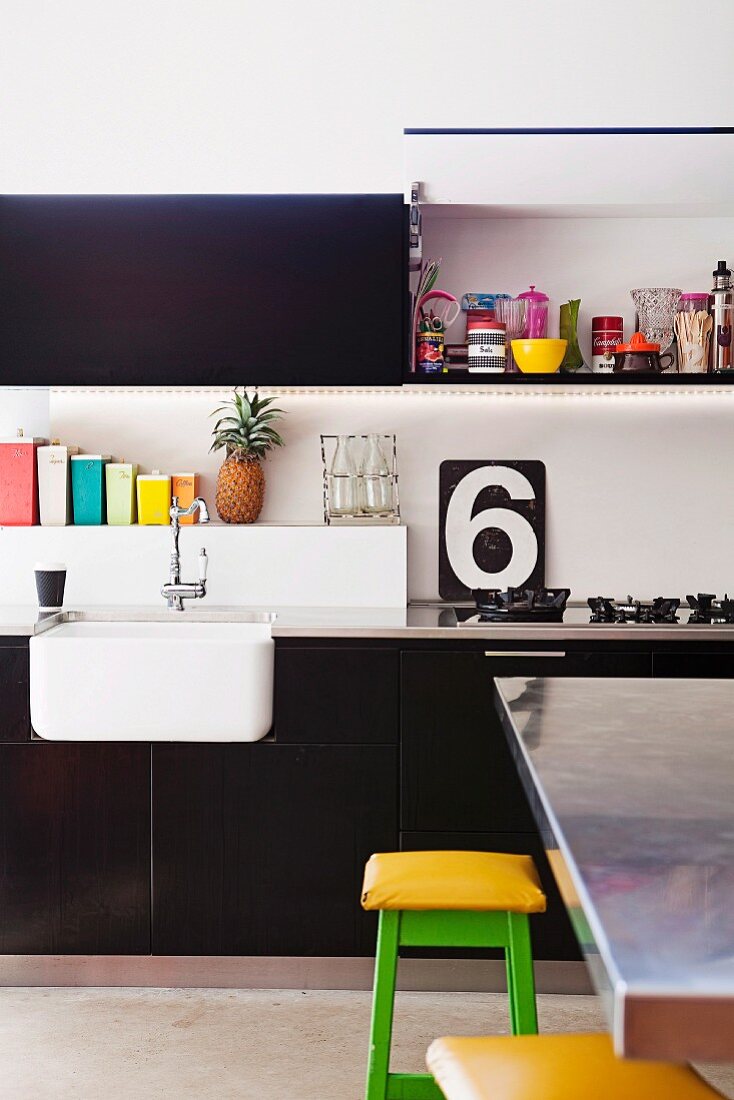 Fitted kitchen with black units, stainless steel worksurfaces, colourful accents and shelf above sink