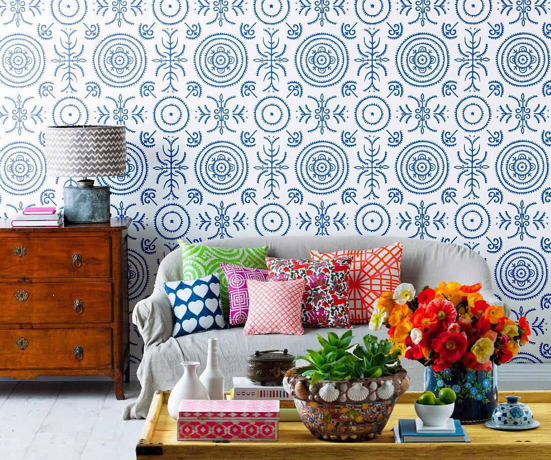 Colourful mixture of scatter cushions on sofa against wallpaper with pattern of blue and white circles