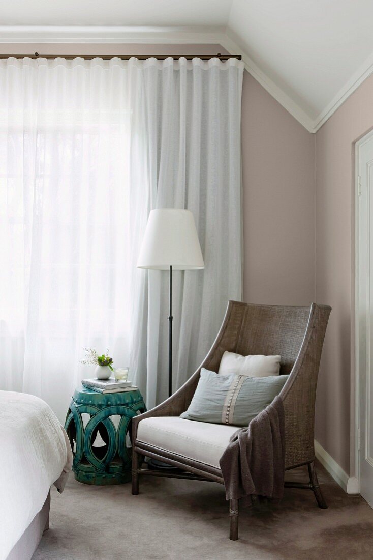 Sessel, Beistelltisch und Stehlampe vor geschlossenem Vorhang in elegantem Schlafzimmer