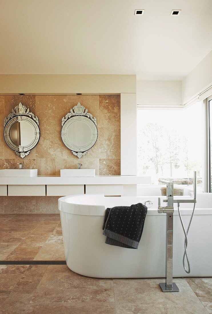Freistehende Wanne in marmorgefliestem Badezimmer; Waschtisch unter runden Spiegeln im verzierten Antikstil