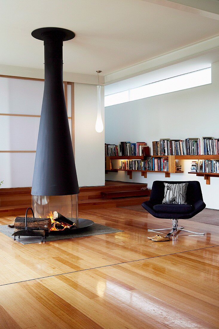 Swivel chair in front of suspended fireplace; two rows of illuminated bookcases and transom window in background