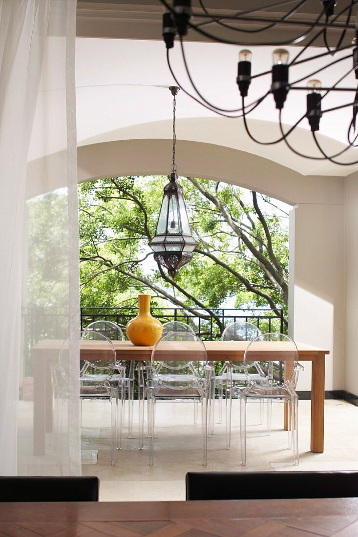 Blick von Esstisch mit schwarzem Kronleuchter auf Essplatz mit postmodernen Acrylglas-Stühlen in überdachtem Innenhof