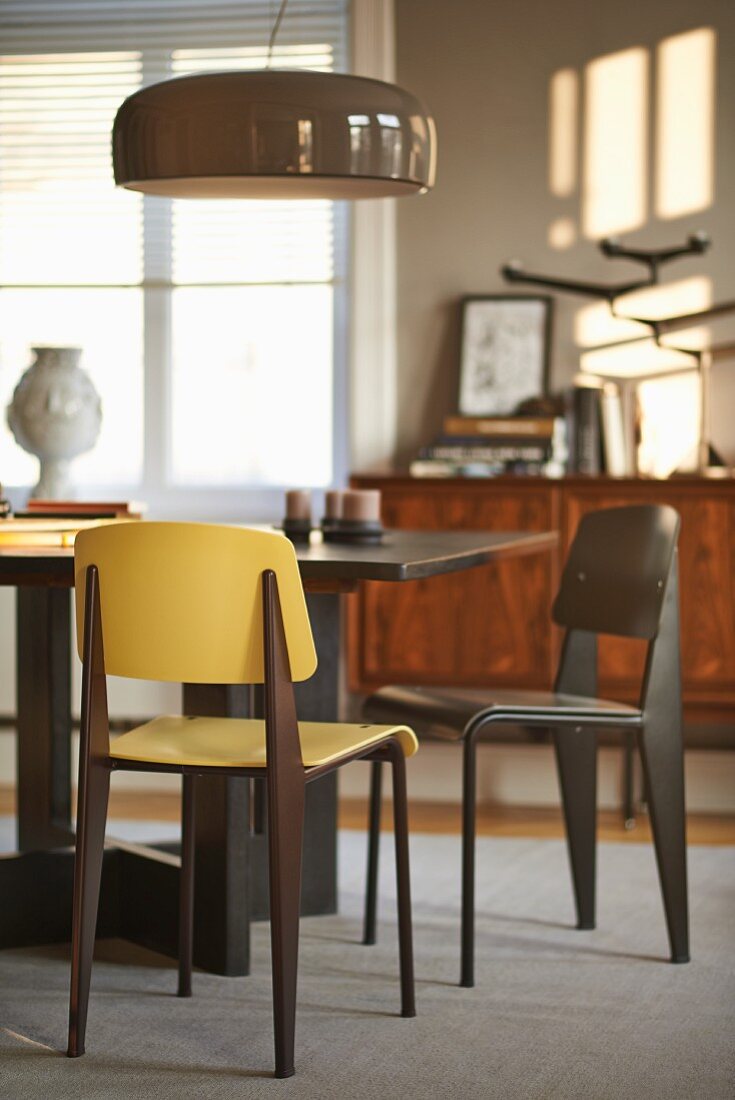 Moderner Esstisch mit Stühlen unter glänzender Hängelampe in sonnigem Esszimmer mit grauen Wänden