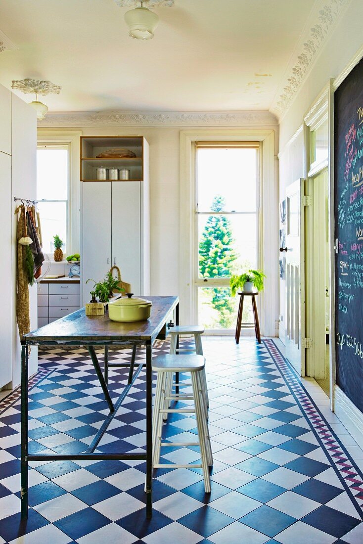 Küche mit schlichtem Metall-Küchentisch und Barhockern auf diagonal verlegten Fliesenboden mit Schachbrettmuster