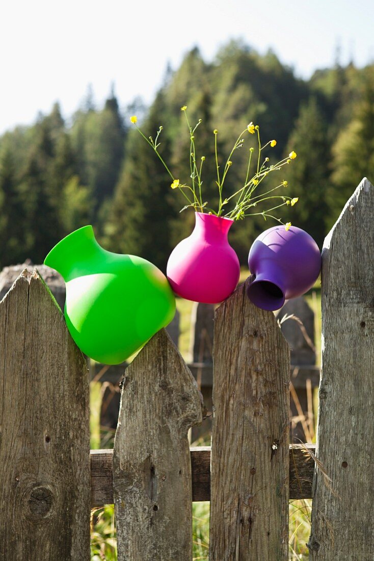 Plastic vases in neon colours on weathered wooden fence