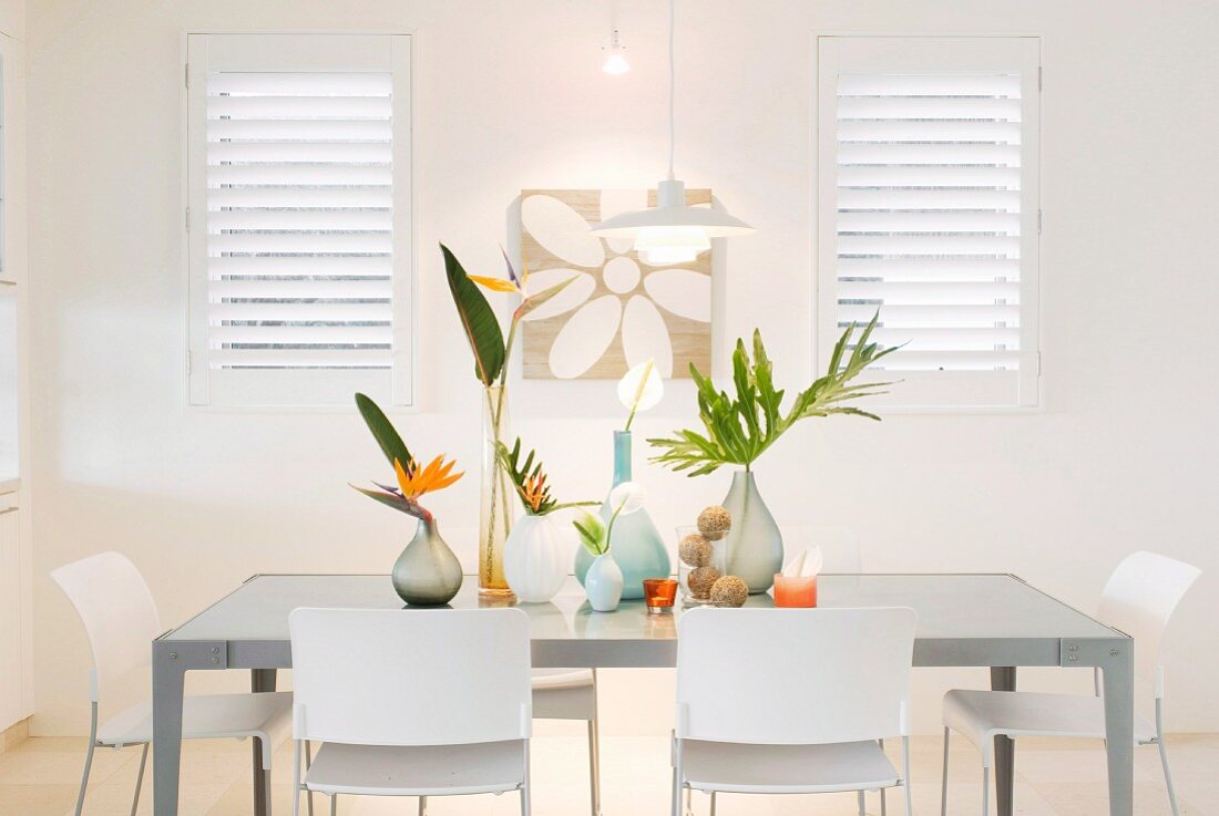 White chairs and various vases of bird-of-paradise flowers and palm fronds in brightly-lit dining area