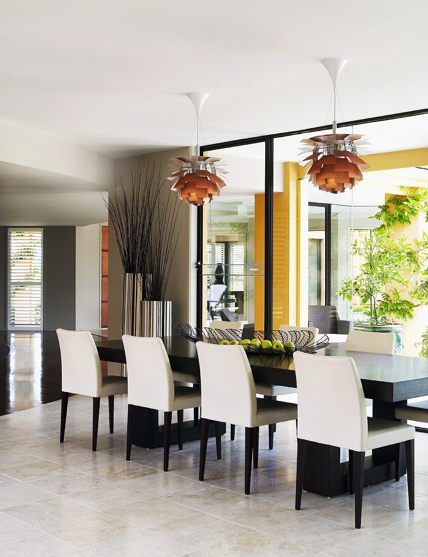 Elegant black and white dining chairs around long table below Bauhaus pendant lamps next to glass wall