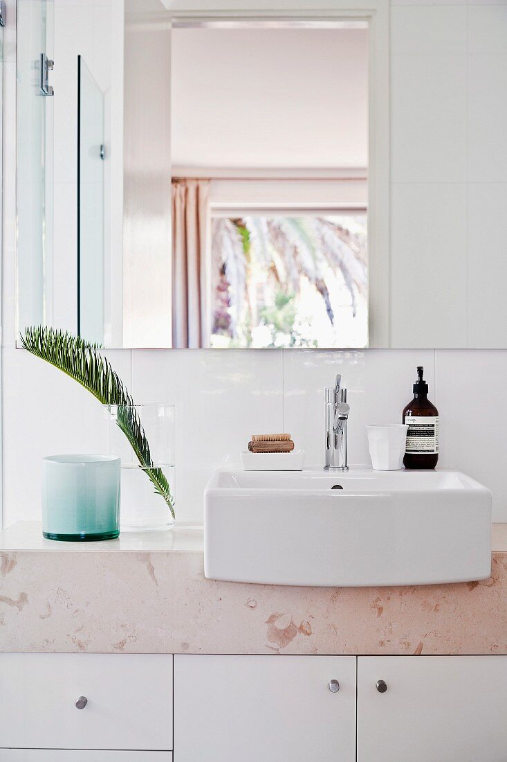Modern washstand with stone top, base cabinets, white countertop sink and palm frond in vase