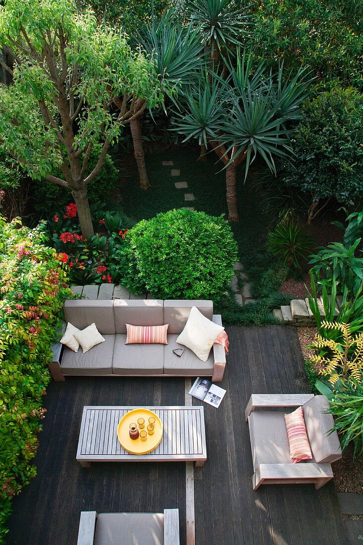 Blick von oben auf Holzterrasse mit moderner Sitzgruppe zwischen dicht bepflanztem Garten