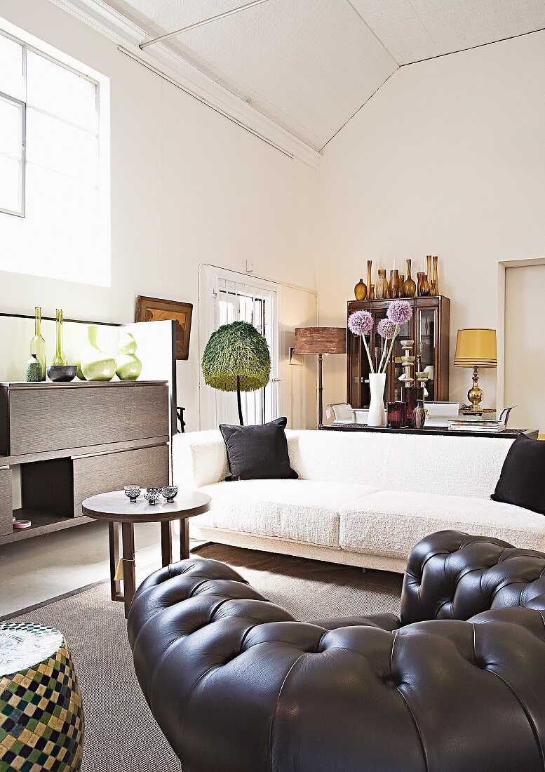 Black leather armchair, white sofa and African occasional furniture in spacious interior