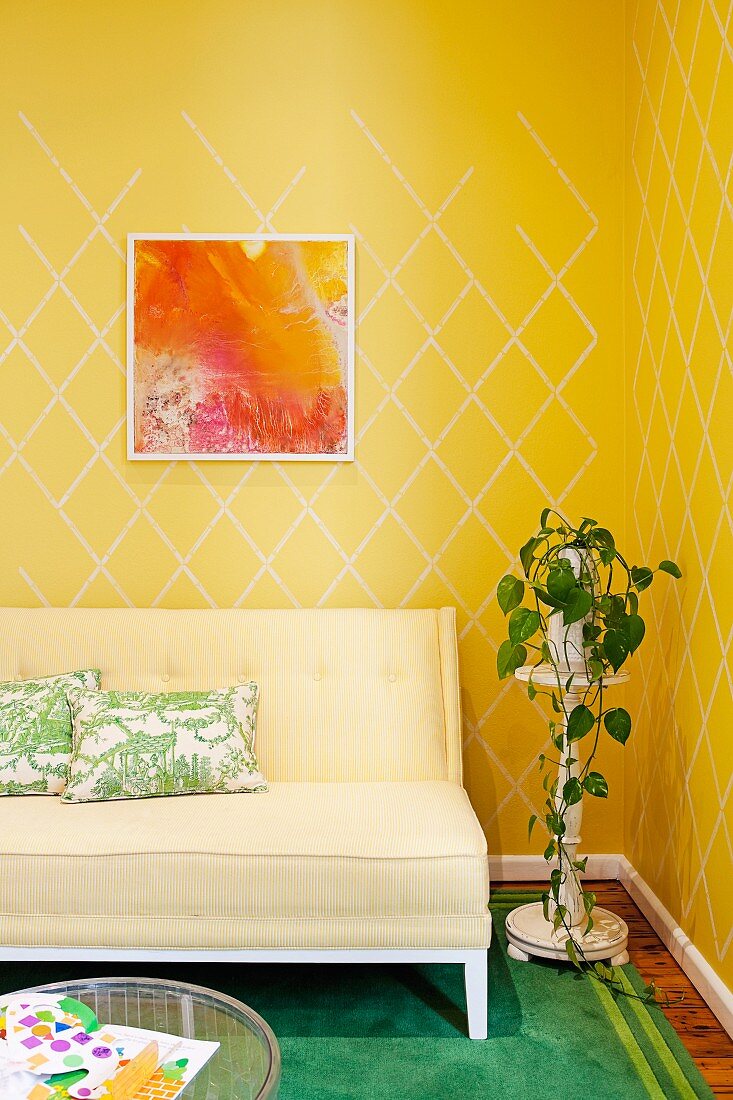 Couch with pale upholstery next to potted plant on plant stand against wall with yellow patterned wallpaper