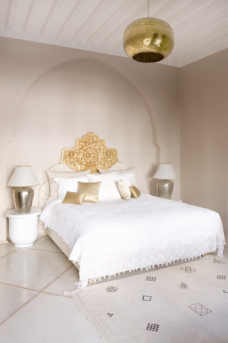 Elegantes, weisses Schlafzimmer mit Doppelbett vor Wandnische in orientalischer Spitzbogenform