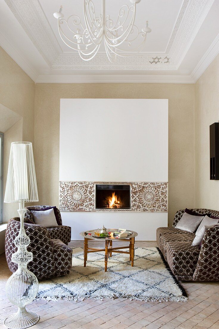 Sofa set and coffee table on rug in front of open fire in elegant ambiance