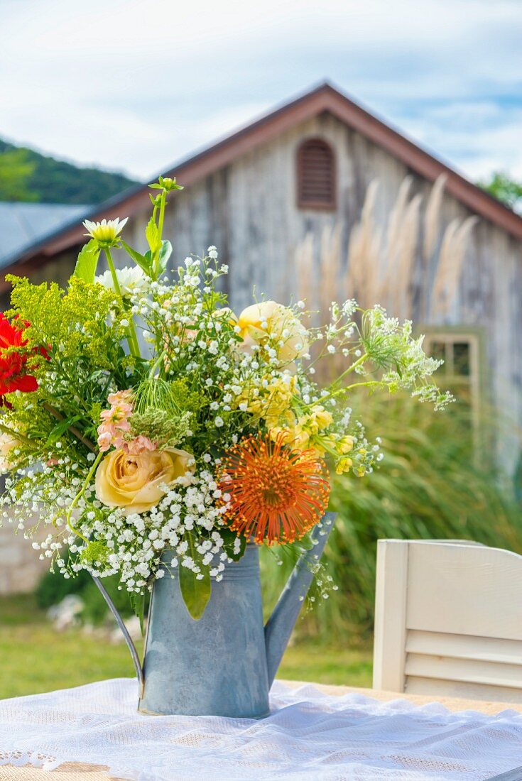 Summery bouquet in metal watering can on table in garden
