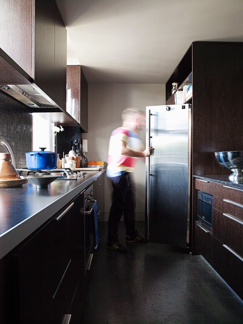 Person in front of fridge in narrow, galley kitchen with two opposite worksurfaces