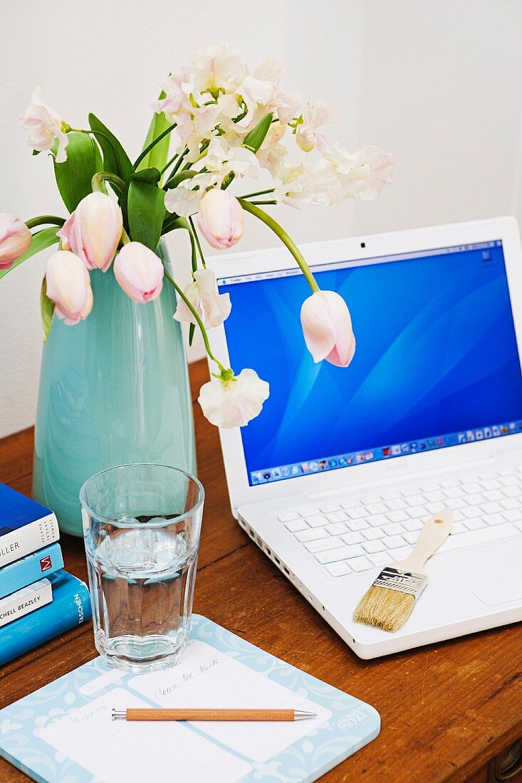 Tulpenstrauss neben Laptop und Wasserglas auf rustikalem Holztisch