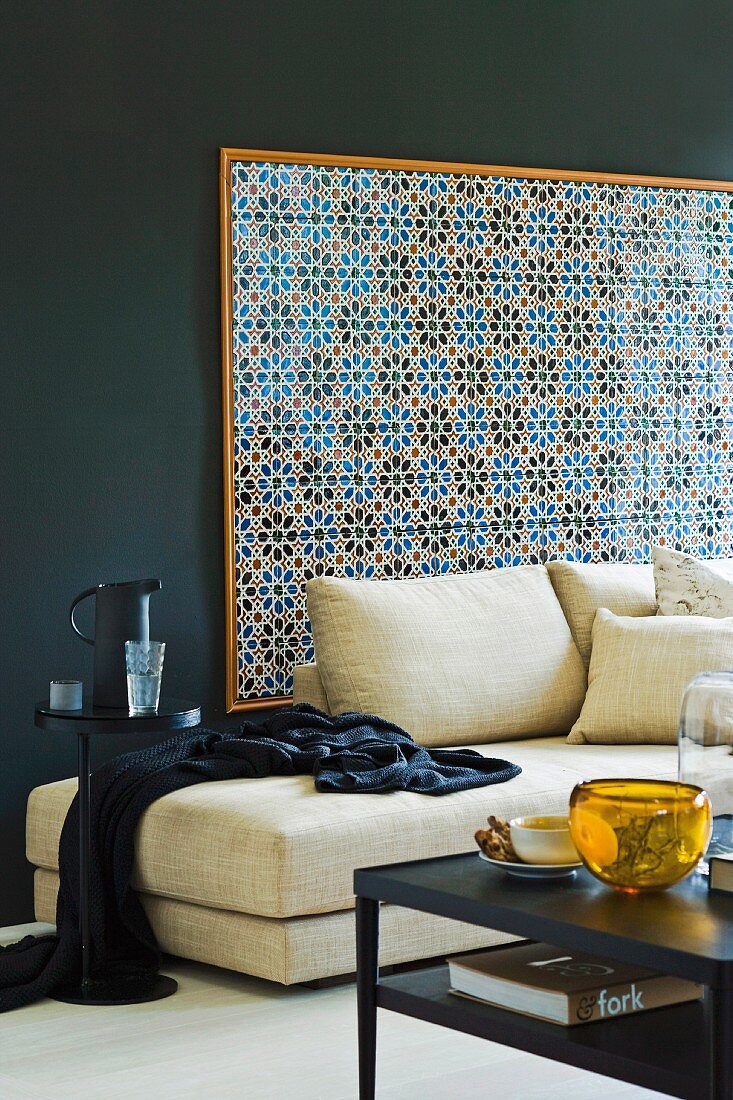 Partially visible coffee table and pale sofa against dark wall with framed tiled panel