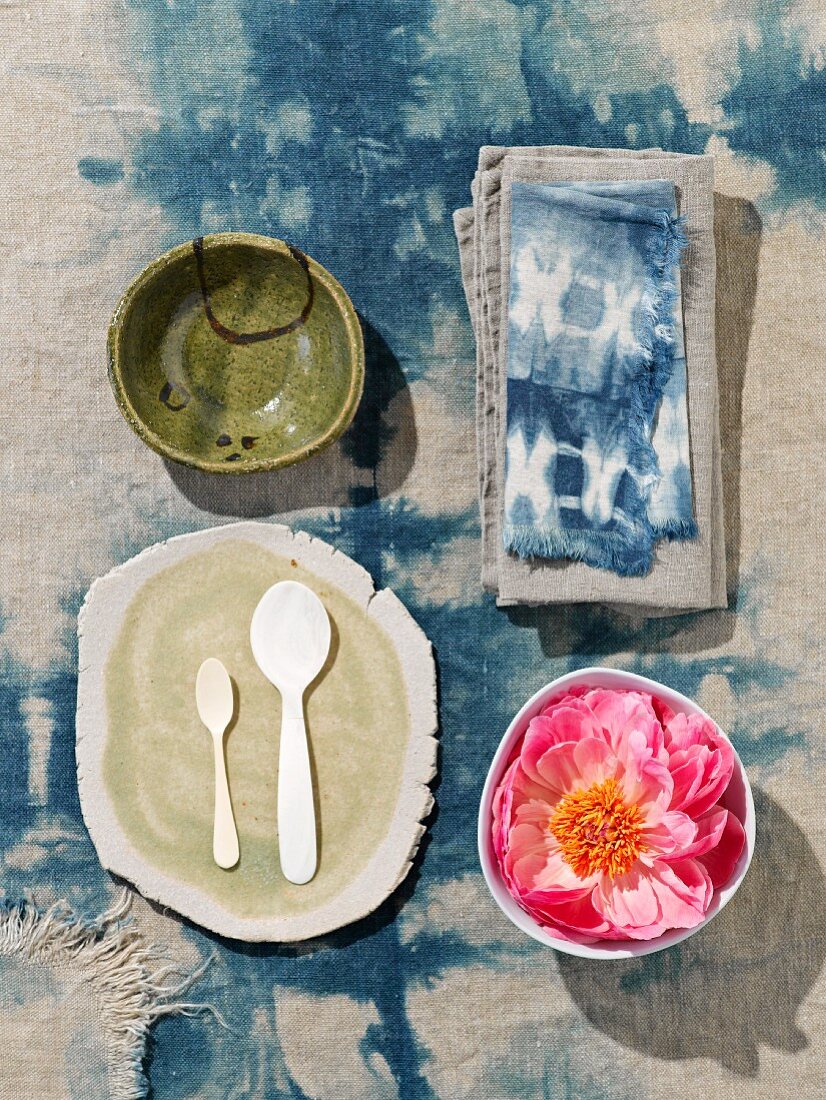 Blick auf weiße Löffel und handgefertigte Platte neben Schale mit Blüten auf Batik Tischtuch