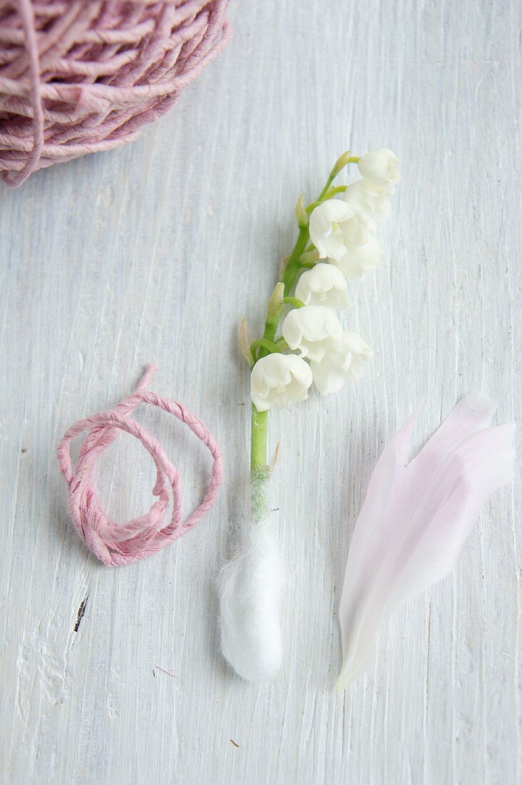 Maiglöckchenstiel mit Watte umwickelt, zwischen rosa Wollfaden und Pfingstrosenblütenblatt