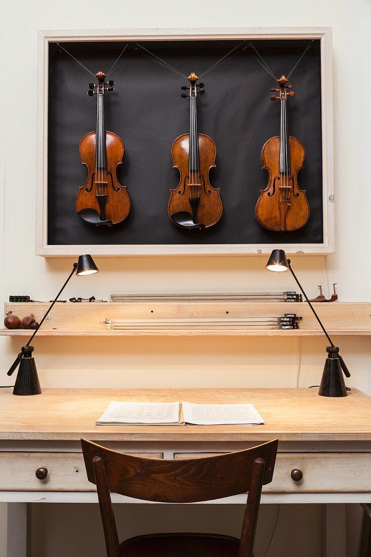 Schaukasten mit drei Geigen über Vintage-Schubladentisch beleuchtet mit zwei modernen Schreibtischlampen