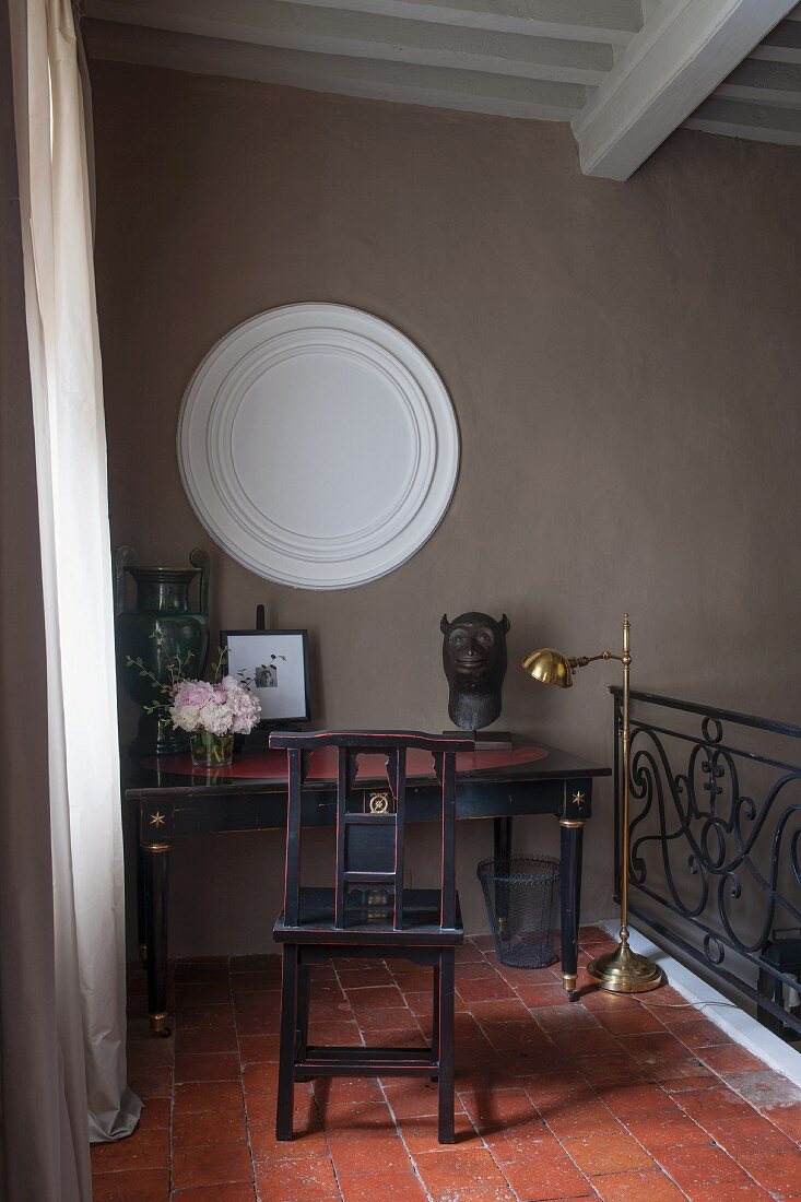 Galerie mit traditionellem Holzstuhl vor Tisch auf Terrakottaboden und rundes Stuckelement an Wand