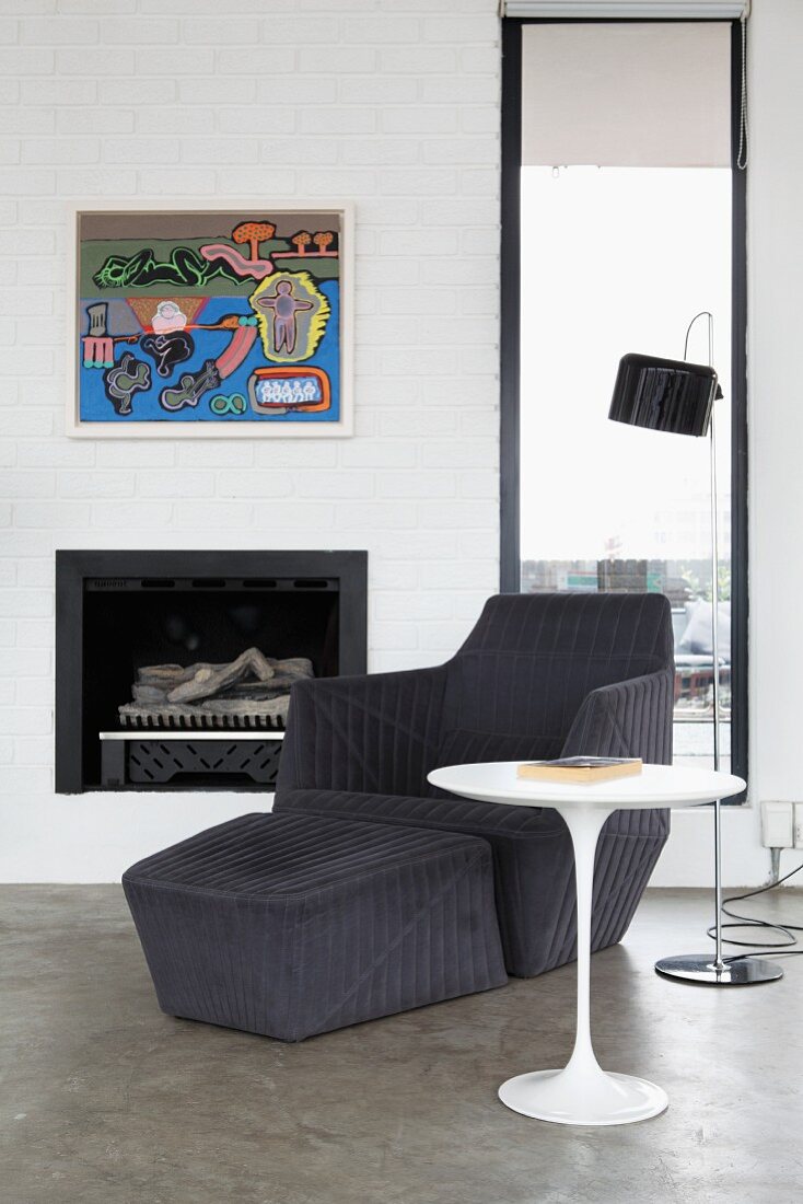 Lounger with footstool and tulip side table in front of modern painting on whitewashed chimney breast