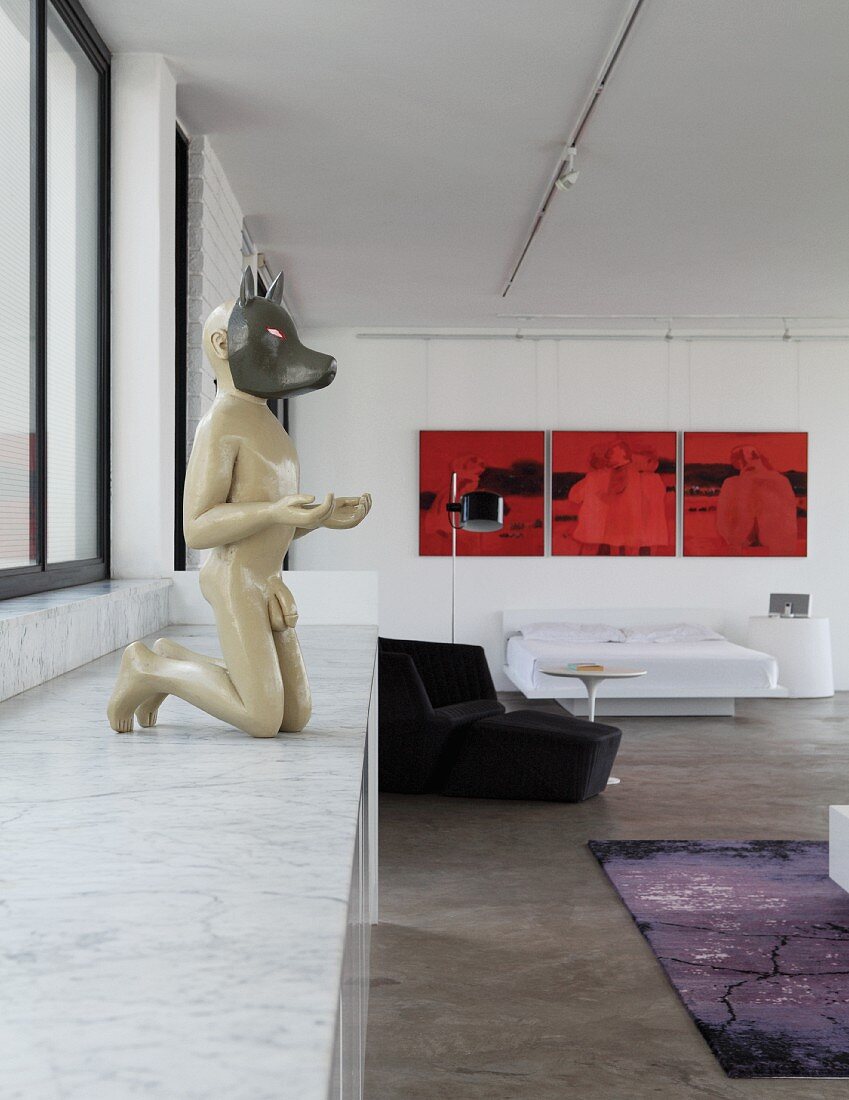 Sculpture of man with animal mask on marble counter with base cabinets and red triptych artwork in loft apartment