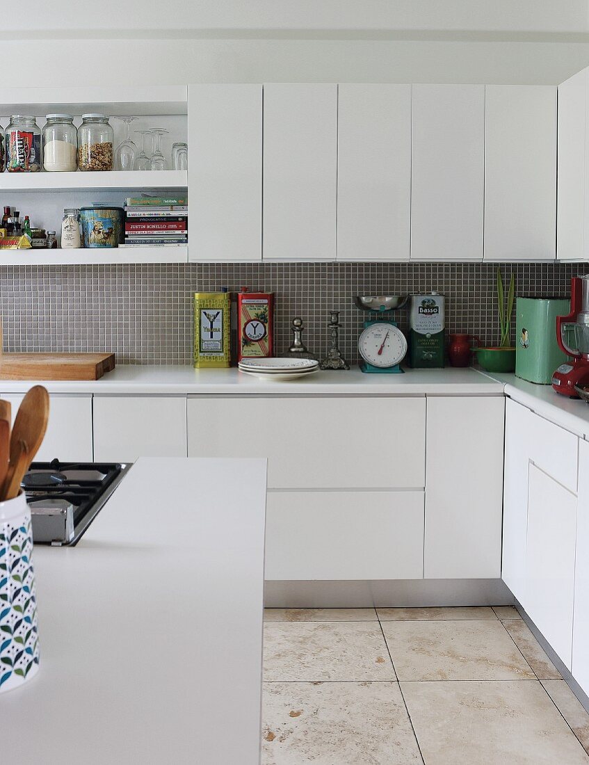 Corner of counter in fitted kitchen with white cabinet doors and sand-coloured stone floor