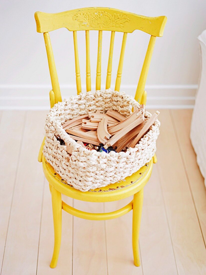 Gelb lackierter Thonetstuhl, auf Sitzfläche geflochtener Korb mit Holzspielzeug