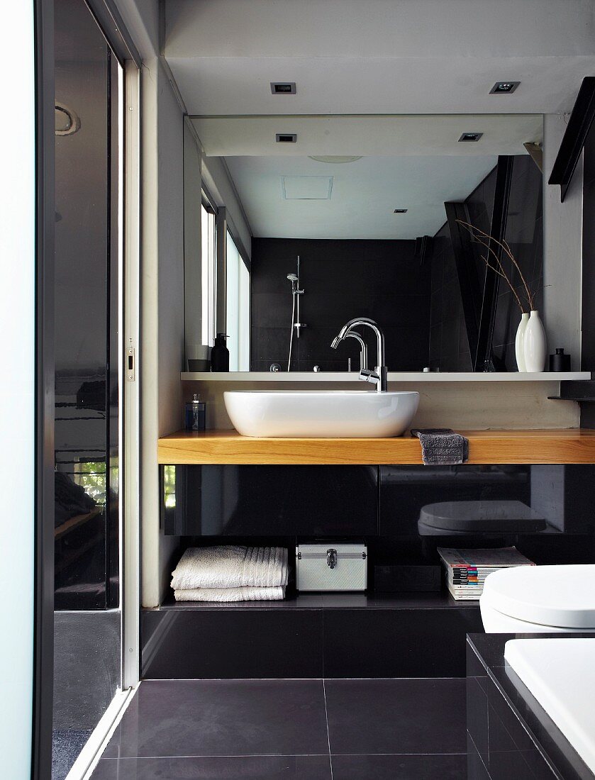 Modern bathroom - wooden washstand with counter-top basin, large mirror and large, black floor tiles