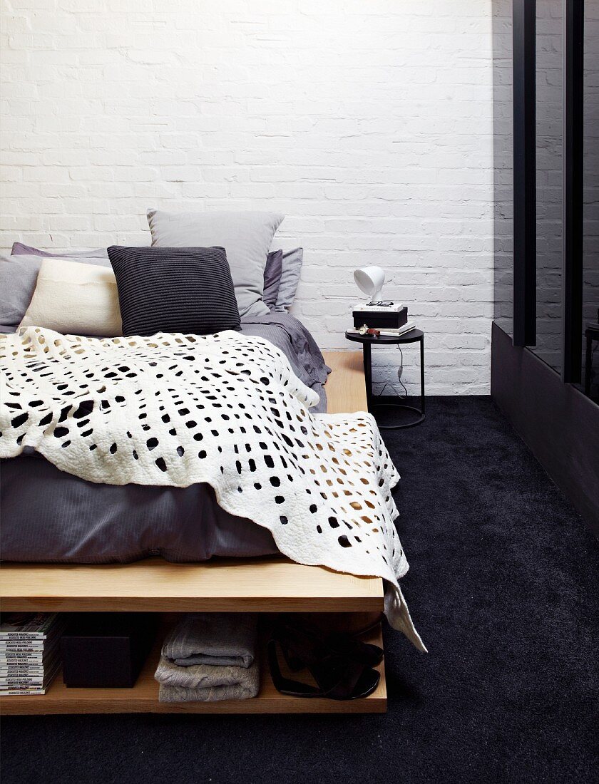 White blanket with pattern of holes on bed with integrated shoe rack on black carpet